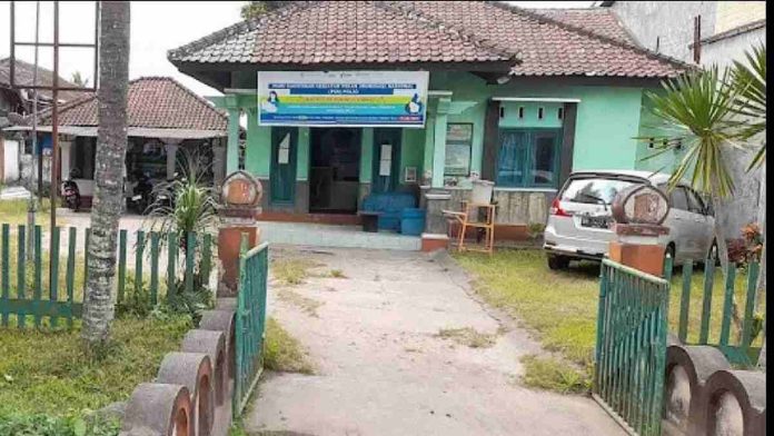 Tampak depan bangunan Kantor Urusan Agama (KUA) Masbagik berwarna hijau dengan spanduk program pemerintah di bagian atas dan sebuah mobil terparkir di halaman.