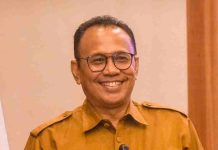 Waspada Pencatutan Nama NTB Care Kini Pengaduan Resmi Beralih ke SP4N-LAPOR Foto potret Dr. H. Ahsanul Khalik, Kepala Dinas Kominfotik NTB, mengenakan seragam dinas cokelat dan kacamata sambil tersenyum ramah di depan latar belakang kayu.