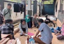 BBPOM Mataram OTT Pengedar Tramadol Ilegal di Lombok Timur Lewat Media Sosial Petugas BBPOM dan kepolisian sedang memeriksa barang bukti paket obat-obatan di teras sebuah rumah bersama beberapa orang yang duduk di lantai.