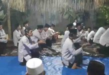 Zikir Saman Tradisi Unik Lepas Keberangkatan Jemaah Calon Haji Lombok Barat Sekelompok pria mengenakan baju koko putih dan peci hitam duduk bersimpuh di atas terpal biru dalam sebuah prosesi zikir tradisional di malam hari.