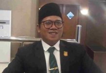 DPRD Mataram Dukung Lima Hari Sekolah, Zia Urrahman: Waktu Eskul Jadi Lebih Panjang! Foto potret Zia Urrahman mengenakan setelan jas hitam, kemeja putih, dasi hijau bermotif, dan peci hitam sedang tersenyum ke arah kamera dalam ruangan.