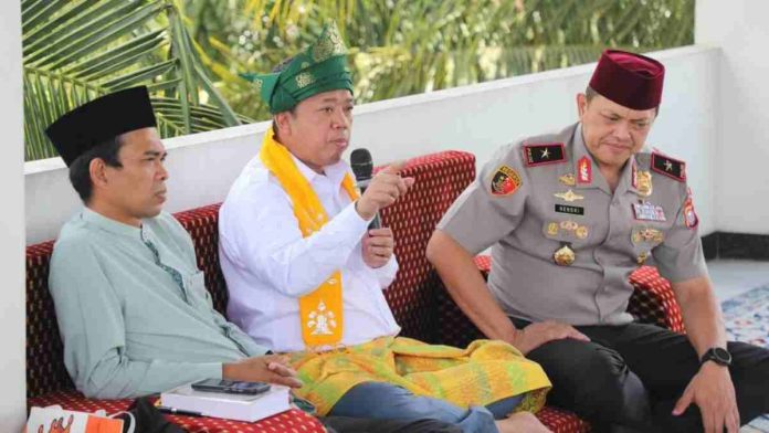 Menteri Nusron Wahid memakai busana melayu putih dan tanjak hijau sedang memegang mik, duduk di antara Ustaz Abdul Somad dan Wakapolda Riau Brigjen Pol Hengki Haryadi.