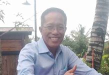 Sekda Lotim Pastikan Anggaran Pilkades Serentak 2026 Sudah Aman Foto potret H. Muhammad Juaini Taofik mengenakan kemeja biru muda, berkacamata, sedang tersenyum lebar dan memberikan jempol dengan latar belakang pohon kelapa.