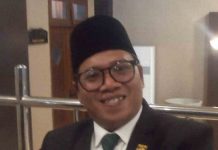 DPRD Kota Mataram Usulkan Tambah Mobil Operasional Dinas Kesehatan Foto potret Zia Urrahman mengenakan setelan jas hitam, kemeja putih, dasi hijau bermotif, dan peci hitam sedang tersenyum ke arah kamera dalam sebuah ruangan formal.