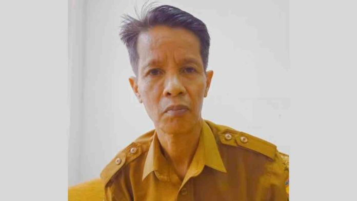 Foto potret Kepala Dinas PMD Lombok Timur Hambali mengenakan seragam dinas cokelat (KHAKI) menghadap kamera dengan latar belakang dinding putih polos.