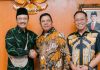 Bupati Lombok Timur Tagih Janji Pusat Terkait Sekolah Rakyat Tiga orang pria berdiri sejajar di depan lambang Garuda Pancasila. Bupati Haerul Warisin berbaju batik hijau bersalaman dengan Mensos Gus Ipul, didampingi Sekda Lotim.