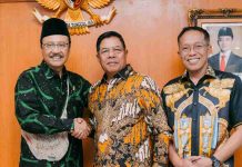 Bupati Lombok Timur Tagih Janji Pusat Terkait Sekolah Rakyat Tiga orang pria berdiri sejajar di depan lambang Garuda Pancasila. Bupati Haerul Warisin berbaju batik hijau bersalaman dengan Mensos Gus Ipul, didampingi Sekda Lotim.
