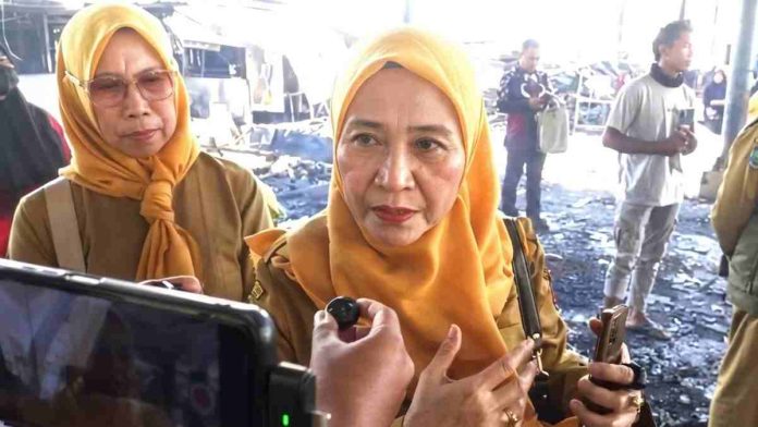 Dua pejabat wanita mengenakan seragam dinas cokelat dan jilbab kuning memberikan keterangan kepada wartawan di lokasi kebakaran pasar yang hangus.