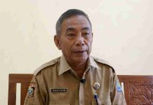 Bursa Sapi Kurban Presiden, Menanti Rekor Satu Ton dari Peternak Lotim Foto setengah badan Haji Mashur mengenakan seragam dinas cokelat (aparatur sipil negara) dengan papan nama "Masyhur" sedang berbicara memberikan penjelasan resmi