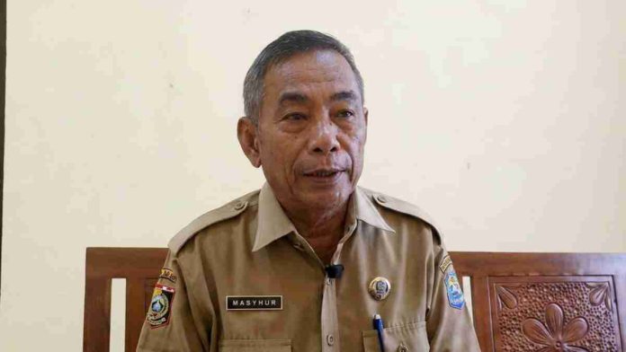 Foto setengah badan Haji Mashur mengenakan seragam dinas cokelat (aparatur sipil negara) dengan papan nama 