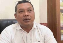 Target Retribusi Sampah Lotara Terganjal Akses Jalan dan Krisis Upah Foto close-up seorang pria paruh baya mengenakan kemeja putih dengan kacamata di atas kepala, sedang berbicara memberikan penjelasan di dalam ruang kantor.