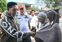 Bupati Lombok Timur Akan Kucurkan Modal Rp 328 Juta untuk Korban Kebakaran Pringgabaya Bupati Haerul Warisin mengenakan jaket hijau gelap dan kacamata hitam sedang bersalaman dengan seorang warga di lokasi pasar, didampingi petugas BPBD berseragam putih.