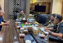BUMD Lombok Timur Setor Dividen Rp 20 Miliar, Pusat Janjikan Dana Insentif Bupati Haerul Warisin dan jajaran duduk berhadapan dengan pejabat kementerian di meja rapat kayu panjang yang dipenuhi hidangan makanan ringan dan minuman.