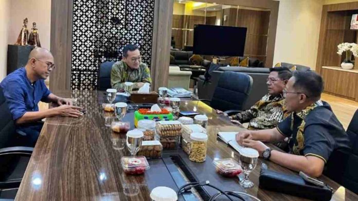 Bupati Haerul Warisin dan jajaran duduk berhadapan dengan pejabat kementerian di meja rapat kayu panjang yang dipenuhi hidangan makanan ringan dan minuman.