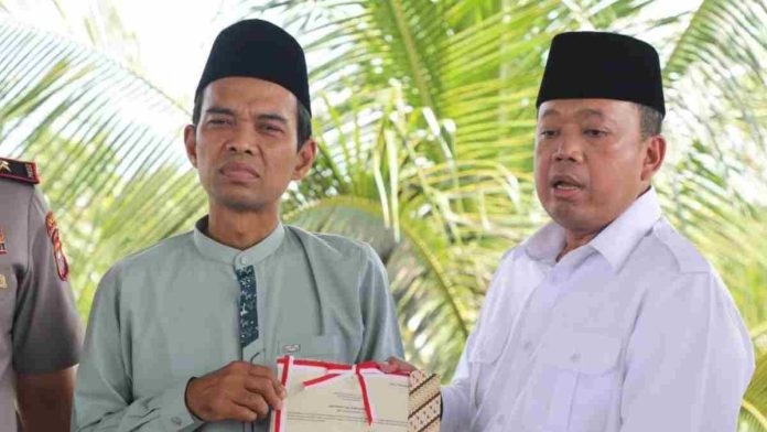 Ustaz Abdul Somad mengenakan baju koko hijau dan peci hitam menerima map sertipikat dari Menteri Nusron Wahid yang berbaju putih dan peci hitam di luar ruangan.