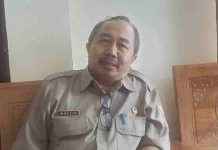 Pemda Lombok Timur Hapus Denda PBB Berlaku Mulai April Hingga Desember Bupati Haerul Warisin memakai jaket hijau gelap dan kacamata hitam sedang menyalami warga di lokasi terbuka, didampingi staf BPBD berseragam putih dan topi oranye.