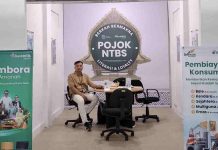 Bank NTB Syariah Hadirkan POJOK NTBS di Pasar Acc Ampenan Mataram Seorang petugas pria duduk di meja layanan POJOK NTBS yang diapit oleh dua banner promosi produk tabungan dan pembiayaan syariah dalam sebuah gerai minimalis.