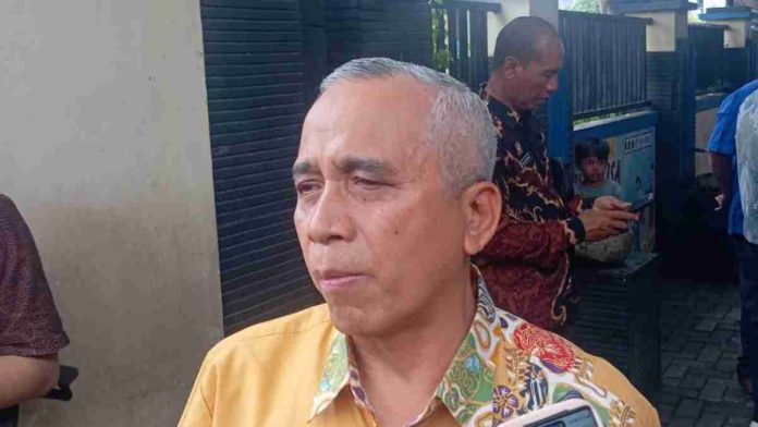 Foto close-up politisi senior Didi Sumardi dengan rambut beruban, mengenakan kemeja batik kuning bermotif, tampak sedang berbicara dengan tatapan serius di luar ruangan.