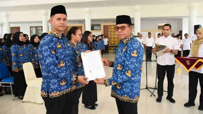 Bupati Lombok Timur mengenakan seragam batik Korpri dan peci hitam sedang menyerahkan map dokumen SK kepada seorang PNS pria yang juga mengenakan seragam batik Korpri serupa.