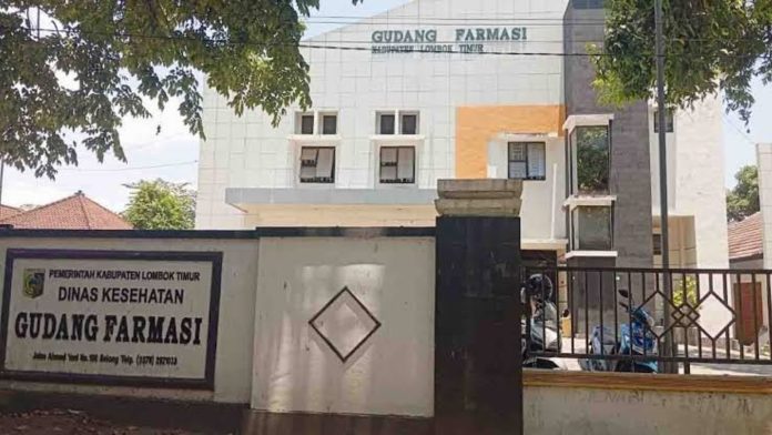 Tampak depan gedung bertingkat Gudang Farmasi Dinas Kesehatan Kabupaten Lombok Timur dengan pagar hitam dan papan nama instansi yang jelas di bagian depan.