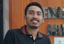 Kuasa Hukum Iqbal: Jangan Pelesetkan Hak Hukum sebagai Kejahatan Foto close-up Firdaus Firmansyah, pria berkumis dan berjanggut tipis mengenakan kaus kerah hitam dengan garis merah-hijau, berlatar belakang dinding kayu bertuliskan "PENGADILAN".