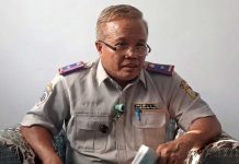Dishub Lombok Timur Bongkar Pemicu Pemborosan Tagihan Listrik PJU Kepala Dinas Perhubungan Safwan mengenakan seragam dinas perhubungan abu-abu dengan atribut lengkap, berkacamata, sedang memberikan keterangan di dalam ruangan.