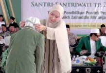 Ketum PBNW Ingatkan Santri NW Anjani Jaga Almamater di Acara Penamatan Seorang wanita berhijab krem sedang mengalungkan medali kepada seorang santri yang membungkuk, dengan latar belakang tamu undangan dan spanduk acara.
