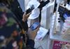 Bank NTB Syariah Sukses Terapkan QRIS Cross Border di Lima Negara Foto jarak dekat tangan seseorang memegang ponsel pintar untuk memindai kode QRIS pada sebuah cetakan kertas di depan gerai minuman UMKM.
