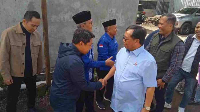 Herman Haeron mengenakan kemeja biru muda logo Demokrat bersalaman dengan pria berjaket biru tua, didampingi jajaran pengurus partai di area terbuka Sembalun.