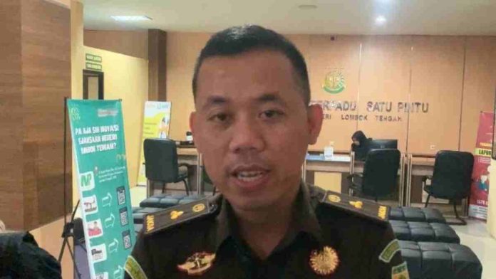 Seorang pria berseragam jaksa berwarna cokelat dengan tanda pangkat sedang berbicara di depan kamera dalam ruangan Pelayanan Terpadu Satu Pintu.