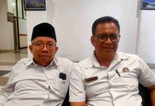 Ketua FKKD Lotim Ancam Segel KUA Masbagik, Kemenag Klaim Masih Tunggu Pusat Foto dua pria duduk berdampingan di dalam ruangan; pria di sebelah kanan (M. Haerul Ikhsan) mengenakan kemeja putih dan kacamata, sementara pria di sebelah kiri mengenakan kopiah hitam.