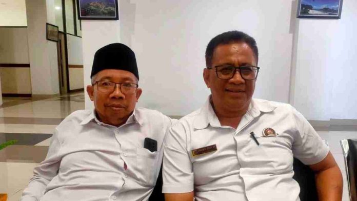 Foto dua pria duduk berdampingan di dalam ruangan; pria di sebelah kanan (M. Haerul Ikhsan) mengenakan kemeja putih dan kacamata, sementara pria di sebelah kiri mengenakan kopiah hitam.