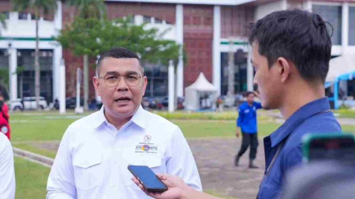 Wakil Menteri ATR Ossy Dermawan mengenakan kemeja putih berlogo kementerian, sedang berbicara di depan wartawan di sebuah lapangan terbuka.