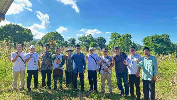 Sepuluh orang pria berdiri berjejer di lahan pertanian jagung yang luas dengan latar belakang langit biru cerah, menunjukkan pose kebersamaan usai panen.