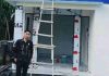 Direktur PDAM Lombok Timur Tinjau Progres Kantor Unit Cabang Suela Seorang pria berdiri di depan bangunan baru Kantor PDAM Unit Suela yang sedang tahap penyelesaian, tampak tangga kayu bersandar pada dinding dan papan nama kantor berwarna biru.