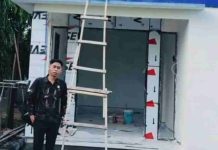 Direktur PDAM Lombok Timur Tinjau Progres Kantor Unit Cabang Suela Seorang pria berdiri di depan bangunan baru Kantor PDAM Unit Suela yang sedang tahap penyelesaian, tampak tangga kayu bersandar pada dinding dan papan nama kantor berwarna biru.