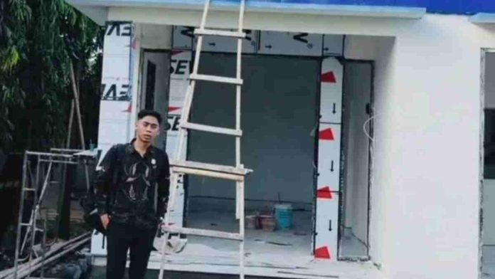 Seorang pria berdiri di depan bangunan baru Kantor PDAM Unit Suela yang sedang tahap penyelesaian, tampak tangga kayu bersandar pada dinding dan papan nama kantor berwarna biru.