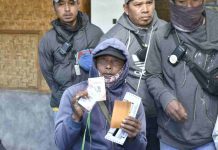 Ojek Wisata Gunung Rinjani Kini Layani QRIS Cross Border Bank NTB Syariah Seorang pria mengenakan jaket hoodie ungu menunjukkan kartu QRIS dan dokumen aktivasi merchant di depan rekan-rekannya sesama penyedia jasa ojek wisata.