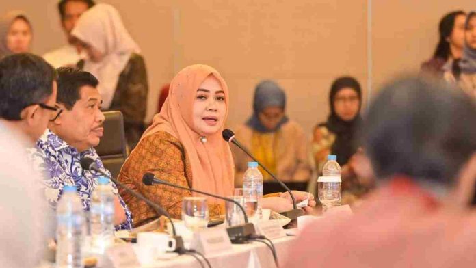 Wakil Gubernur NTB Hj. Indah Dhamayanti Putri mengenakan hijab oranye dan batik cokelat, duduk di meja pimpinan rapat berdampingan dengan Wamendagri Bima Arya dalam sebuah forum resmi.
